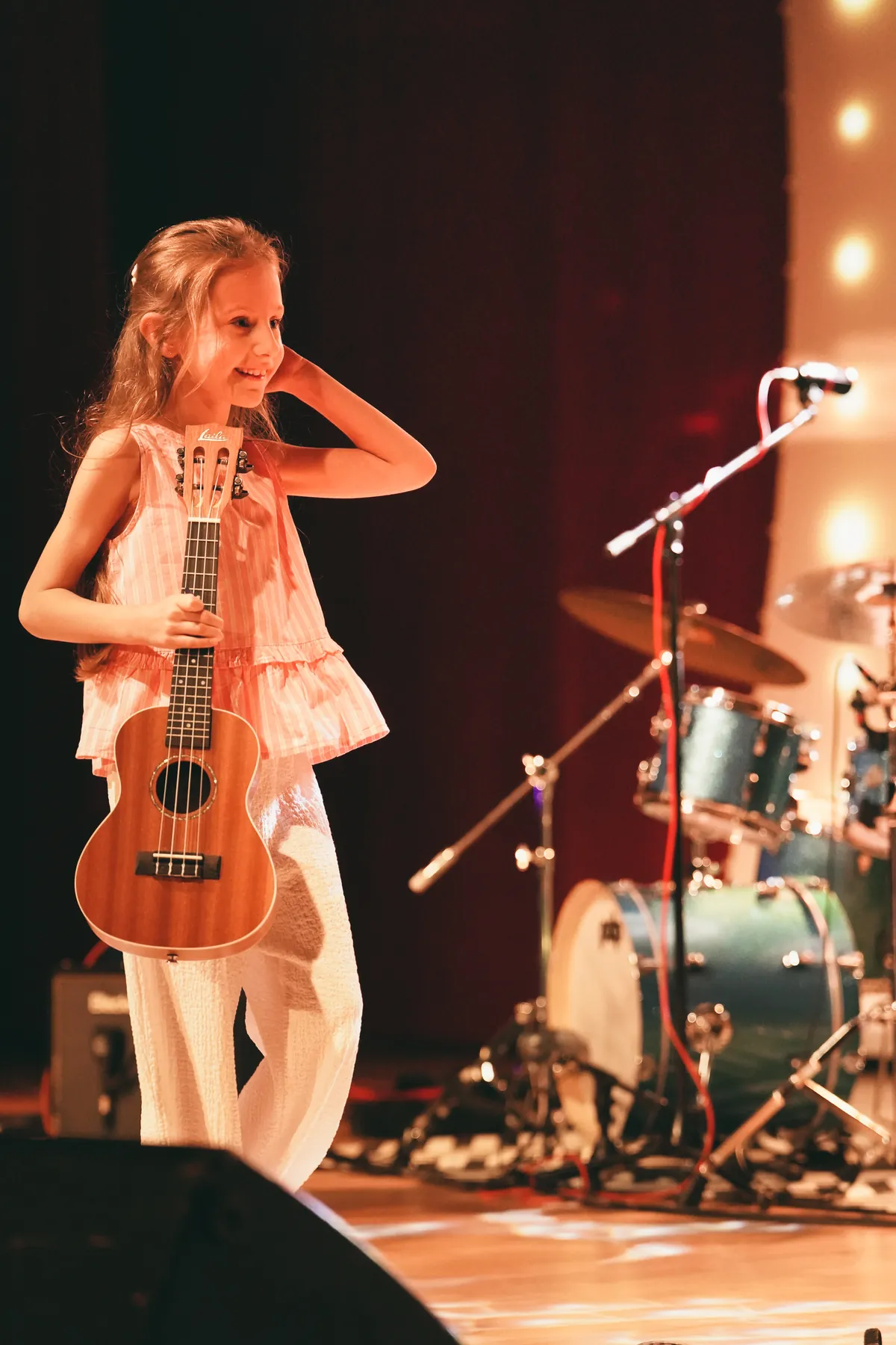 Dziecko z ukulele na scenie podczas koncertu szkoły
